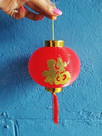 Close-up of hand holding red umbrella against blue wall