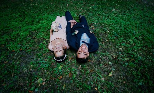 High angle view of bride and bridegroom smiling while lying on grassy field