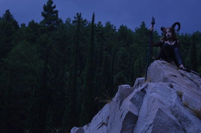 Woman in costume sitting on cliff at dusk