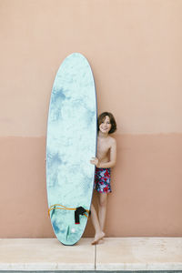 Boy standing with surfboard in front of wall