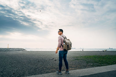 Rear view of man standing on beach against sky