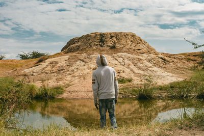 A man standing infront of water looking at a big rock object