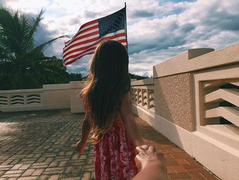 Cropped hand holding girl against american flag at building terrace