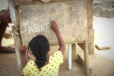 High angle rear view of girl writing alphabets with chalk on wood
