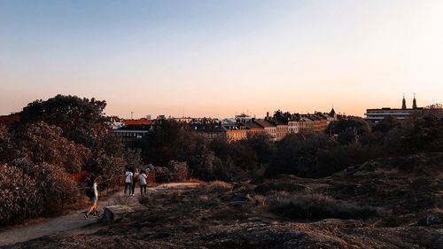 People by trees against sky during sunset in city