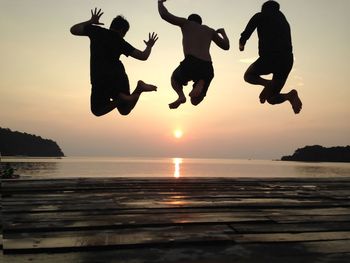 Silhouette people jumping on beach against sky during sunset