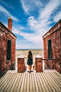 Rear view of woman standing by sea against sky