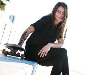 Portrait of young woman sitting by skateboard