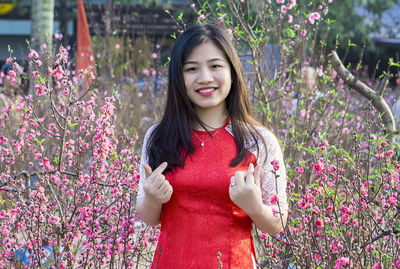 Portrait of smiling young woman standing against flowers