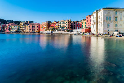 Canal by buildings in city against clear blue sky