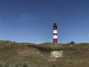 Lighthouse by sea against clear blue sky