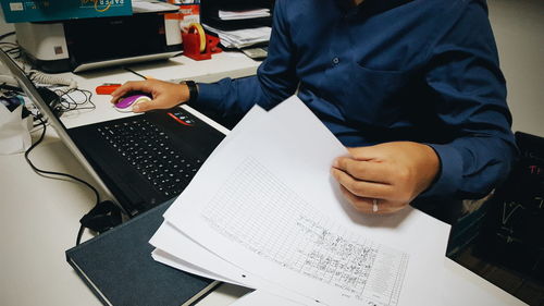 Midsection of businessman working on laptop with documents at desk in office