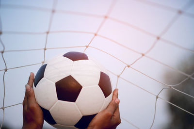 Close-up of hand holding soccer ball by net