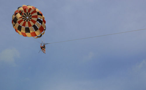 Low angle view of people parasailing against sky