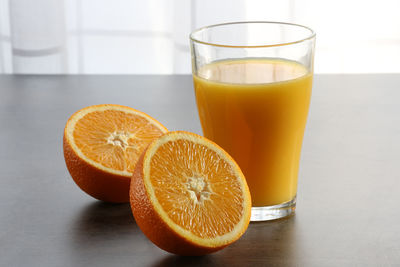 Close-up of halved oranges by juice in glass on table