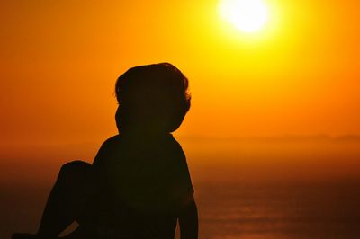 Silhouette boy sitting against sea during sunset