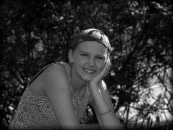 Portrait of smiling young woman sitting against plants in park