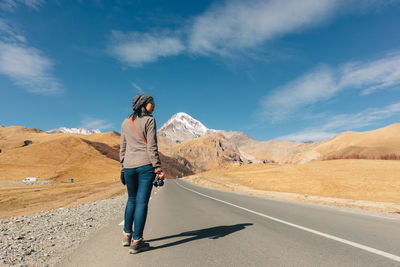 Woman standing on road by mountains against sky