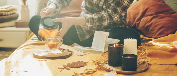 Woman's hand pouring tea in a cup  sitting on bed, reading book, relaxing at home in autumn season.