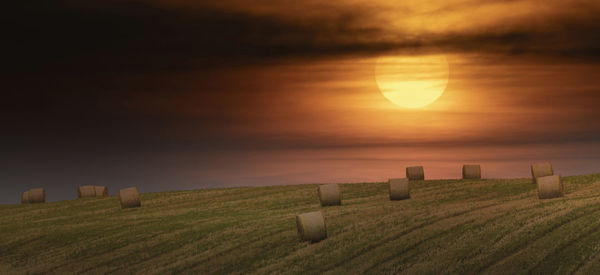 Hay bales on field against sky during sunset