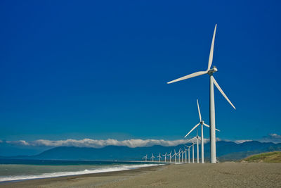 Low angle view of windmill on beach against blue sky