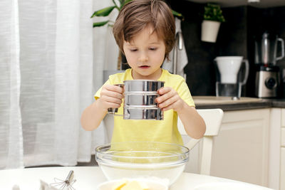 Little cute boy adds flour to the dough. children cook in the kitchen. little chefs