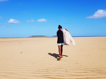 Rear view of girl walking at shore of beach against sky