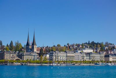 Buildings by sea against clear blue sky