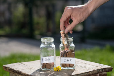 Cropped hand putting money in jar on table