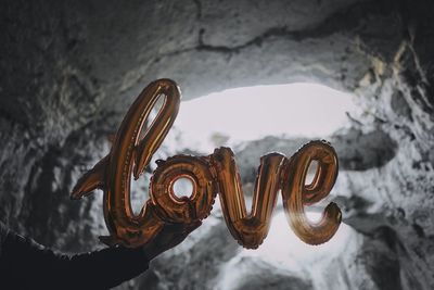 Cropped hand of person holding love text helium balloons against rock formations during winter