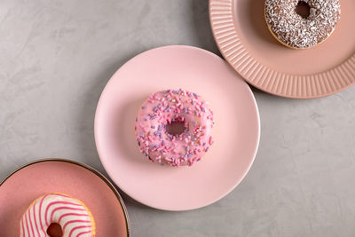 Three glazed donuts lie on tall pink plates on a gray surface. selective focus. view from above.