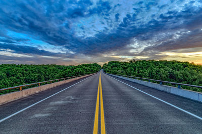 Road leading towards trees against sky