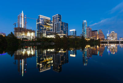 Reflection of illuminated buildings in lake against blue sky