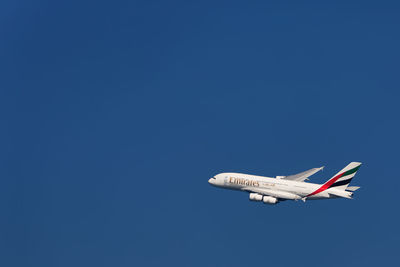 Low angle view of airplane flying against clear blue sky