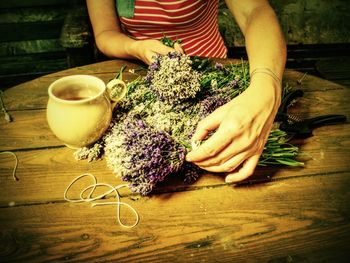 Girl hands with scissors and string preparing lavender flowers bunches on wooden table.