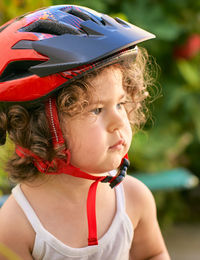 Little girl in a bike helmet is playing in the backyard with plants and watering them