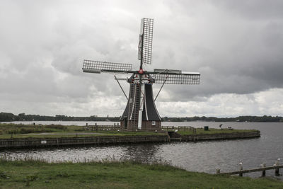 Traditional windmill by river against sky