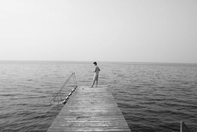 Man standing on pier over sea against sky