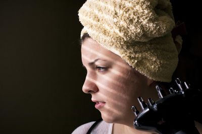 Close-up of woman wearing towel looking away against black background