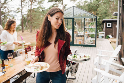 Smiling mid adult woman with leftovers in plate walking against dining table in patio