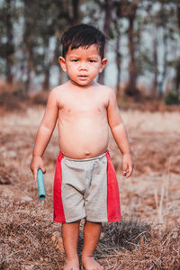 Portrait of cute shirtless boy standing on field