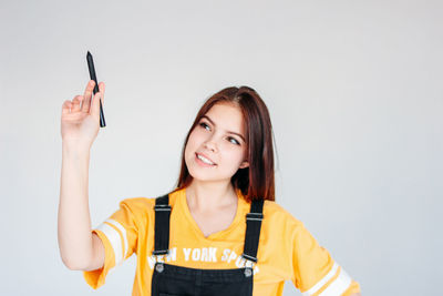 Smiling young woman holding digitized pen against gray background