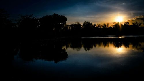 Silhouette trees by lake against sky during sunset