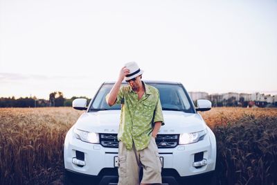 Man holding camera while standing by car on field against sky