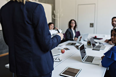 Midsection of businesswoman holding document while discussing with colleagues during meeting in board room