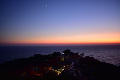 Silhouette buildings by sea against sky during sunset