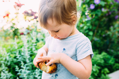 Cute little girl eats a chocolate donut outside in summer