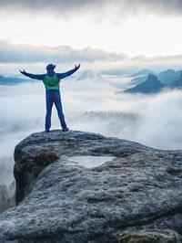 Male hiker finnaly standing on a rock stock and enjoying foggy mountain view