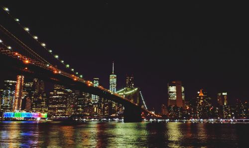 Illuminated bridge over river by buildings against sky at night