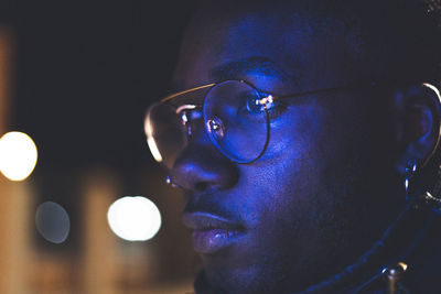 Close-up of man wearing eyeglasses in illuminated city at night